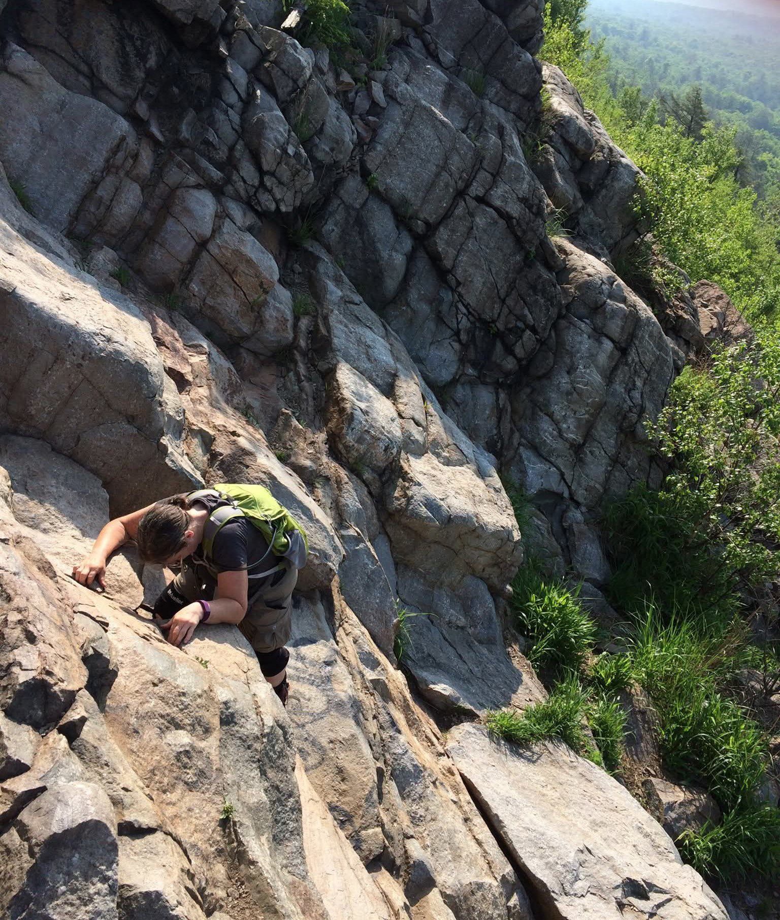 A person in a blue suit smiles outdoors with a desert landscape in the background.